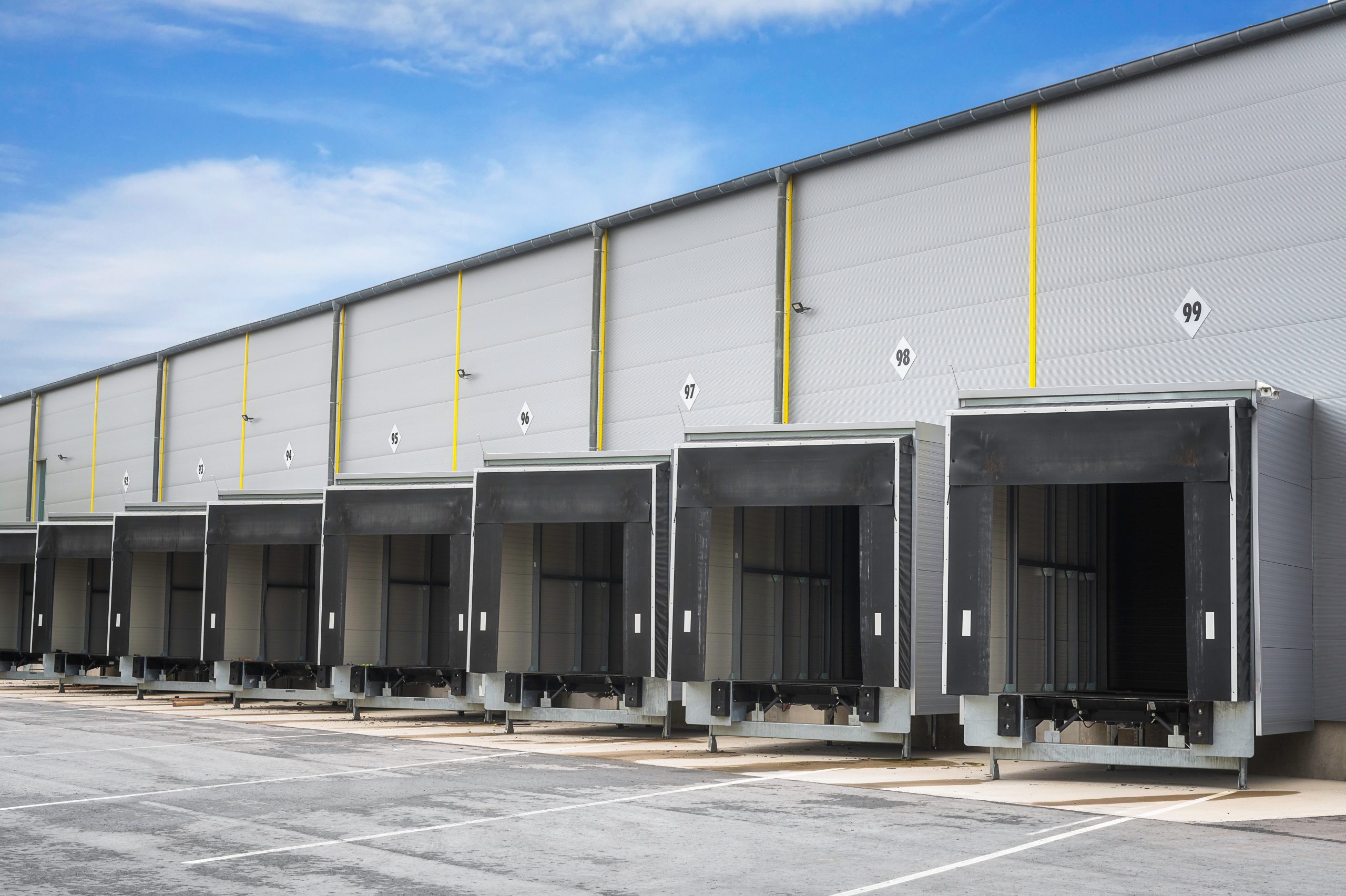 Warehouse loading docks on a sunny day. Open gates of an industrial warehouse. Storehouse doors in a row. Distribution warehouse with open doors.